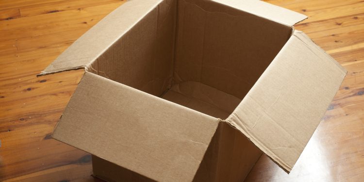 Emptied cardboard box with the flaps open standing on a wooden parquet floor conceptual of packaging, mail, storage, or removals