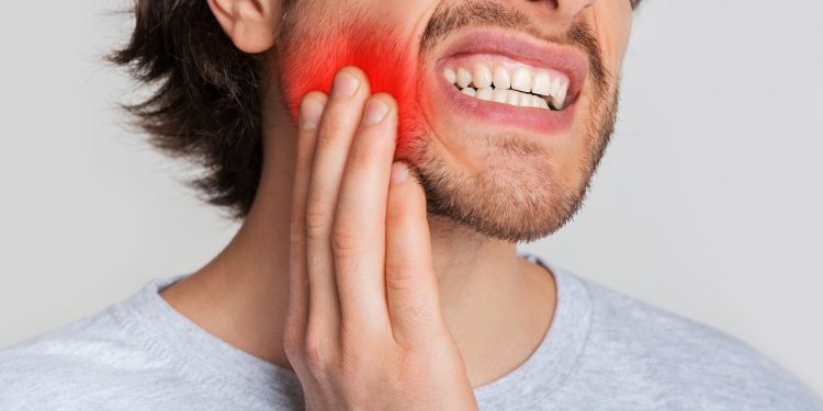 Tooth and gum inflammation. Guy suffers from pain in his mouth and presses hand to red sore spot, panorama, cropped, studio shot