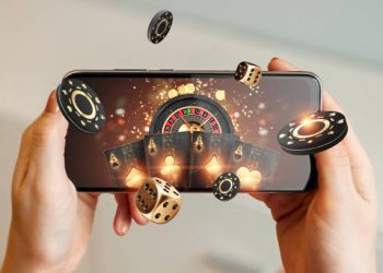 Creative background, online casino, in a man's hand a smartphone with playing cards, roulette and chips, black-gold background. Internet gambling concept. Copy space.
